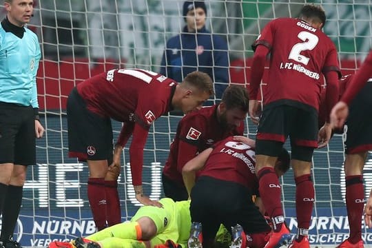 Der Nürnberger Torwart Christian Mathenia (M) liegt verletzt nach einem Zusammenstoß mit einem anderen Spieler auf dem Rasen.