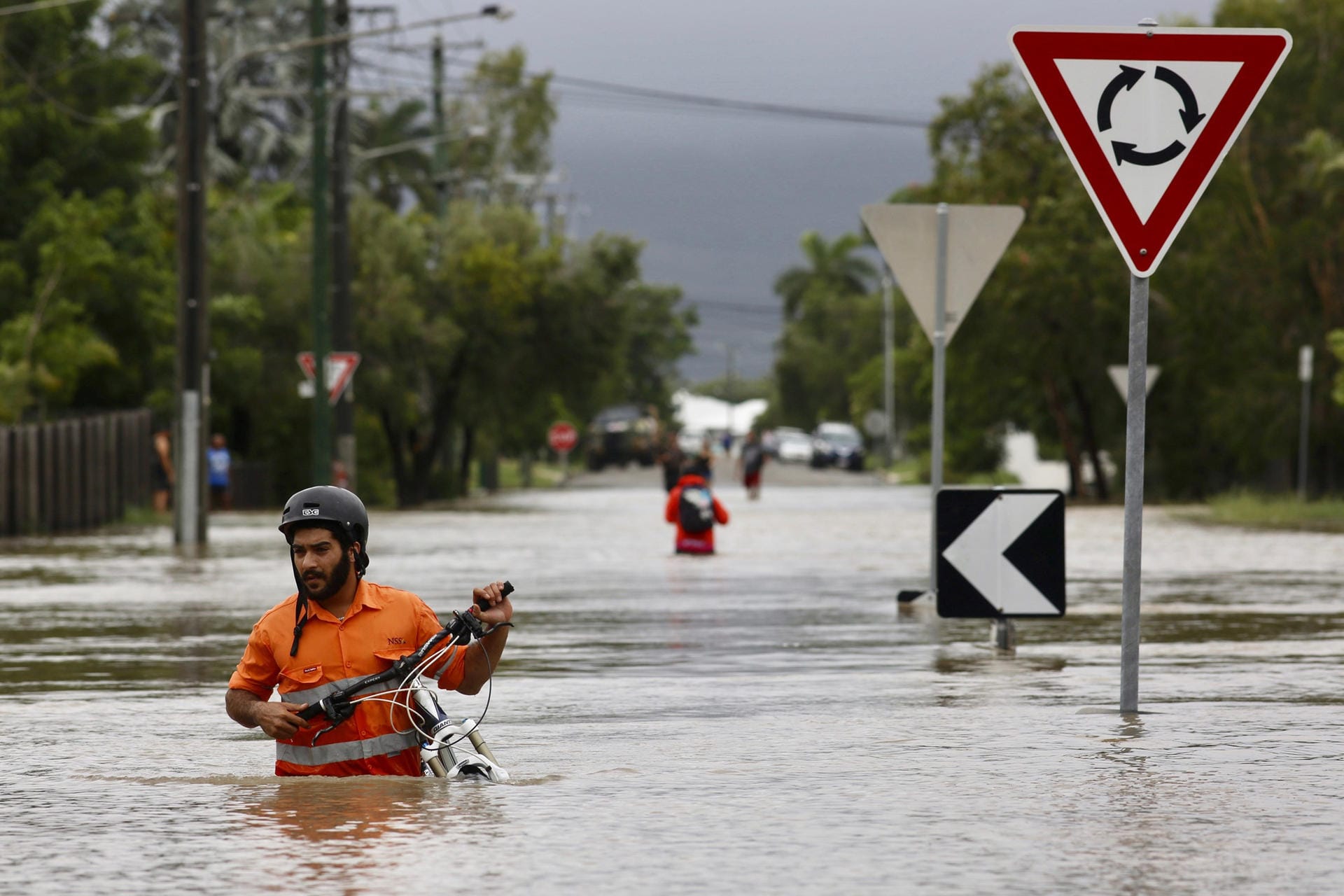 Australien, Townsville: Ein Anwohner schiebt ein Fahrrad durch das Hochwasser im Hermit Park. Der tropische Nordosten Australiens wird von ungewöhnlich heftigem Regen heimgesucht.