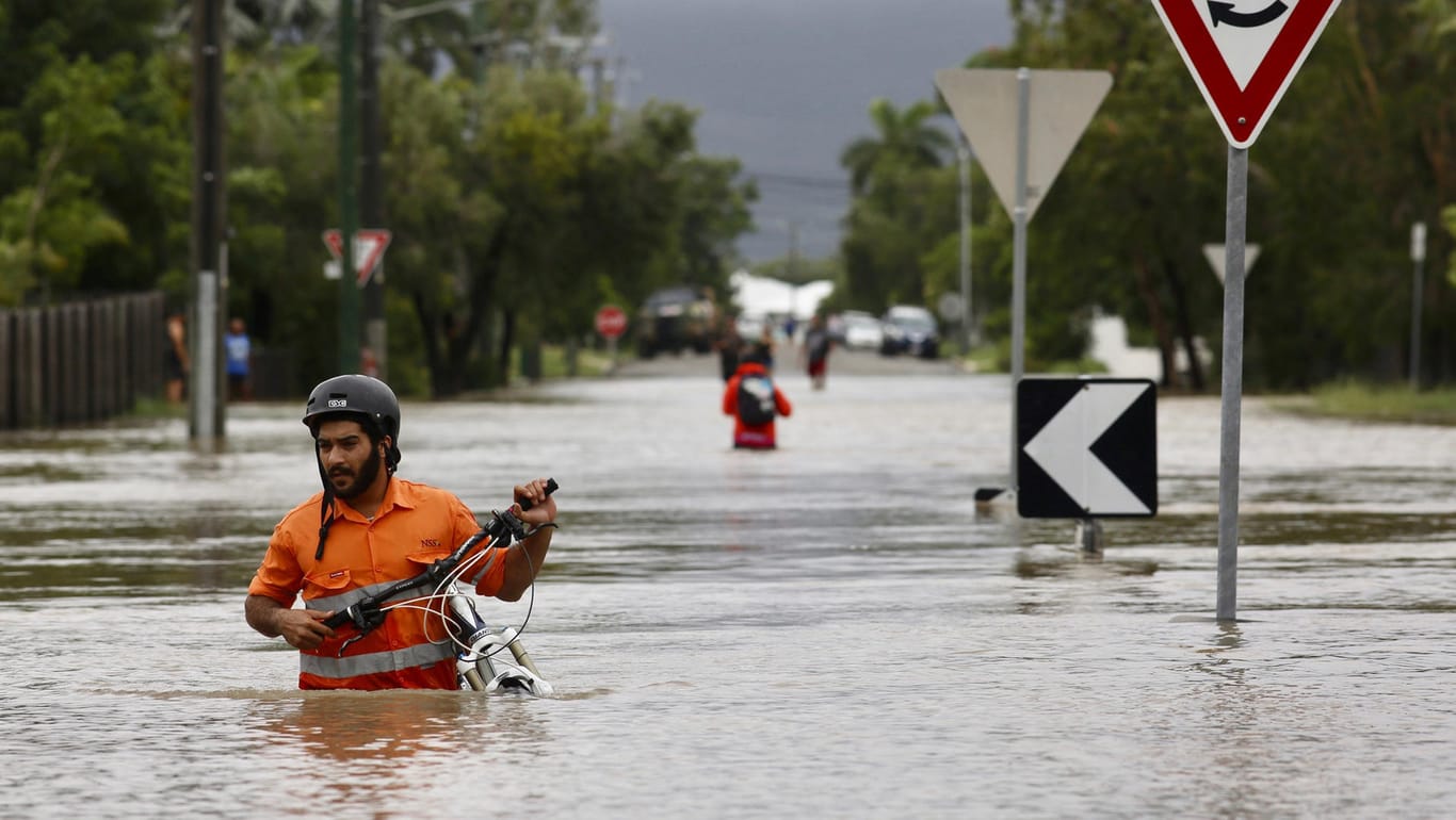 Australien, Townsville: Ein Anwohner schiebt ein Fahrrad durch das Hochwasser im Hermit Park. Der tropische Nordosten Australiens wird von ungewöhnlich heftigem Regen heimgesucht.