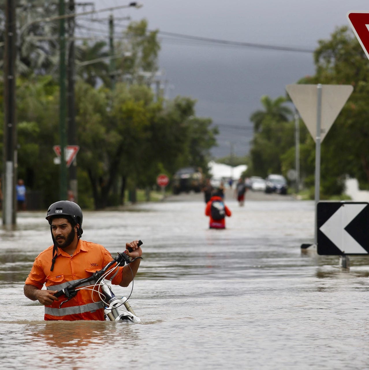 Australien, Townsville: Ein Anwohner schiebt ein Fahrrad durch das Hochwasser im Hermit Park. Der tropische Nordosten Australiens wird von ungewöhnlich heftigem Regen heimgesucht.
