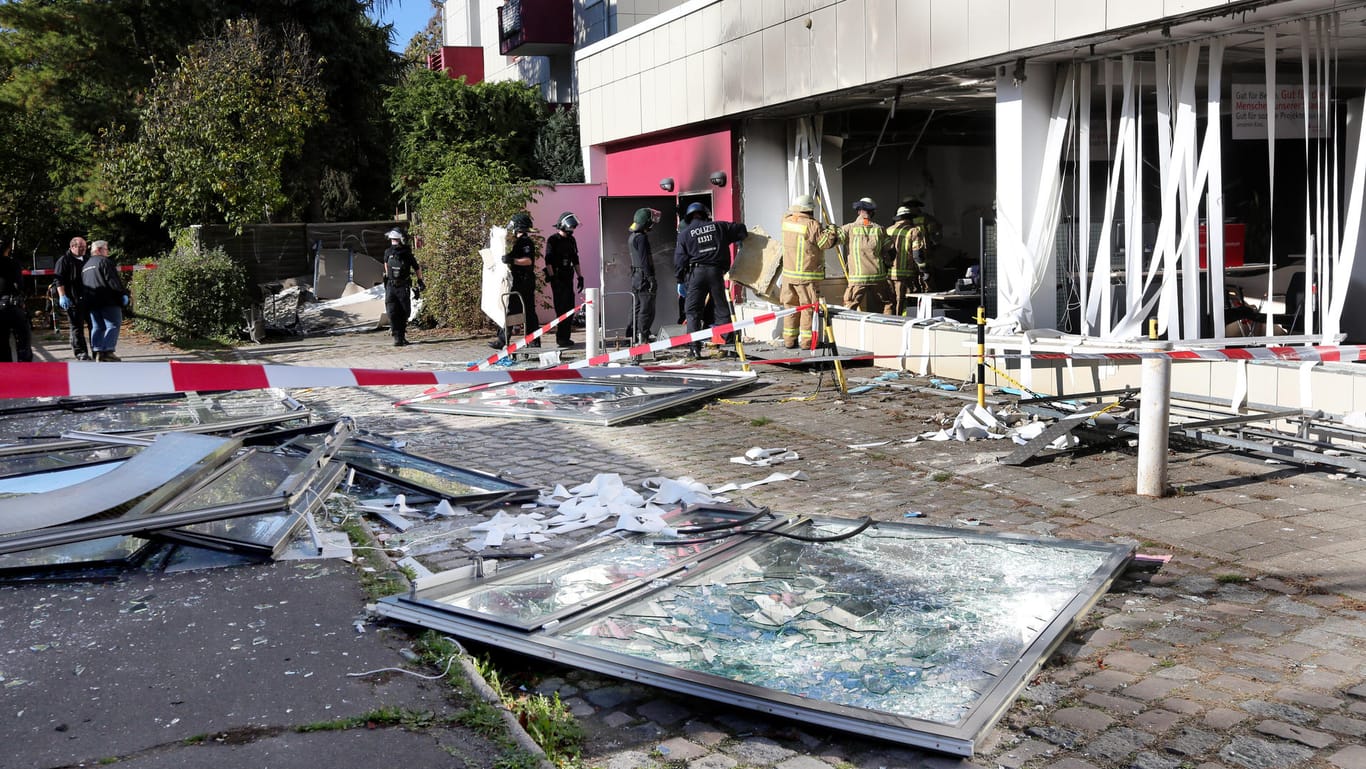 Polizeibeamte und Feuerwehrleute untersuchen die Trümmer vor einer Sparkassenfiliale in Berlin. Unbekannte hatten in den frühen Morgenstunden in der Filiale am Mariendorfer Damm eine Explosion ausgelöst und Schließfächer ausgeräumt.