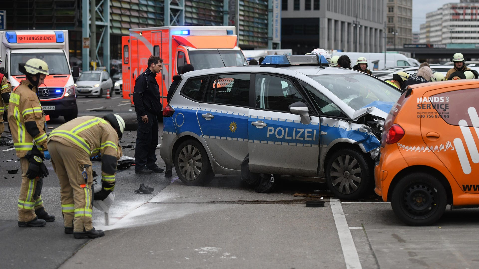 Ein Polizist und Feuerwehrmänner arbeiten an einem Unfallort, an dem ein Polizeifahrzeug mit einem weiteren Auto zusammenprallte.