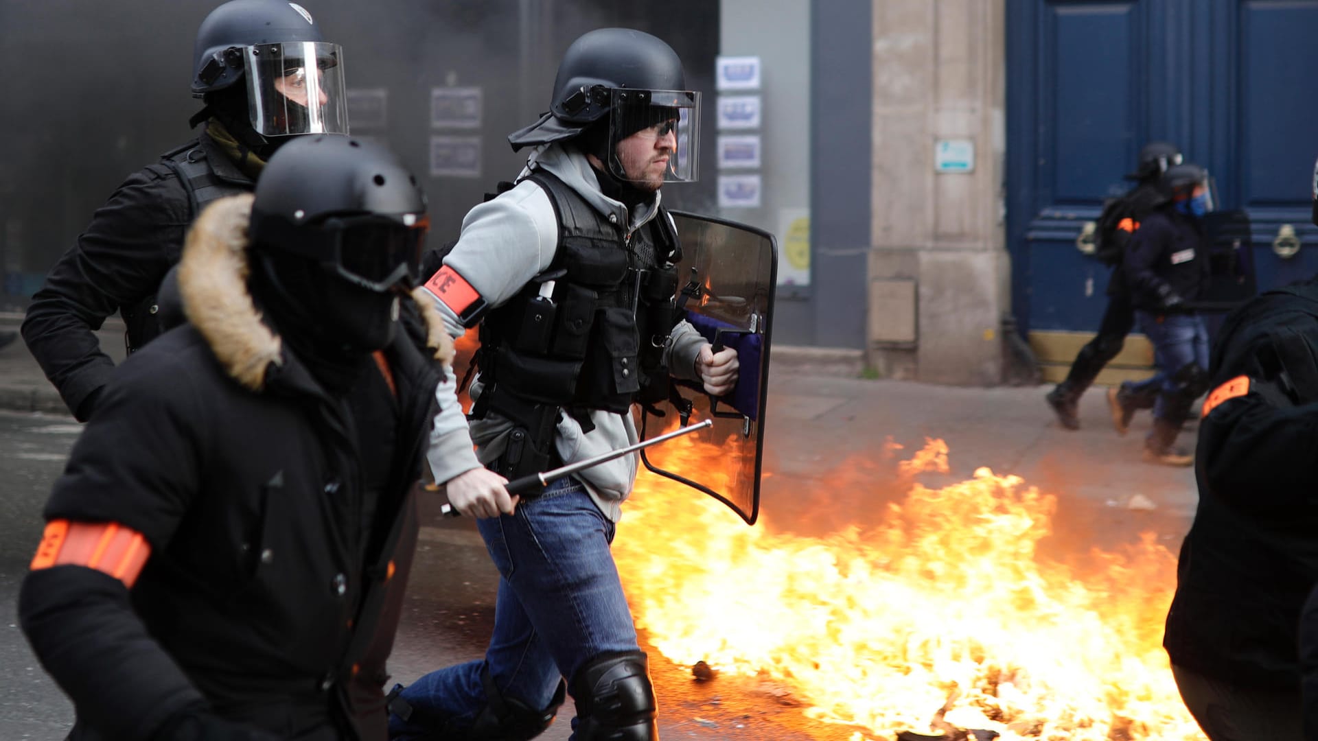 Polizisten laufen an von "Gelbwesten"- Demonstranten in Brand gesetzten Mülleimern vorbei: Einem Fotografen der Aktivisten sollen Teile der Hand abgerissen worden sein.