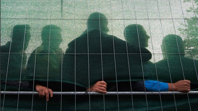 Flüchtlinge hinter dem Zaun einer Flüchtlingsunterkunft.