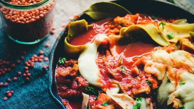 Für die Lasagne werden rote Linsen mit zerkleinerten Nudelplatten in Tomatensaft gekocht.