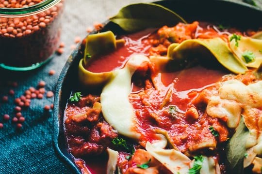 Für die Lasagne werden rote Linsen mit zerkleinerten Nudelplatten in Tomatensaft gekocht.