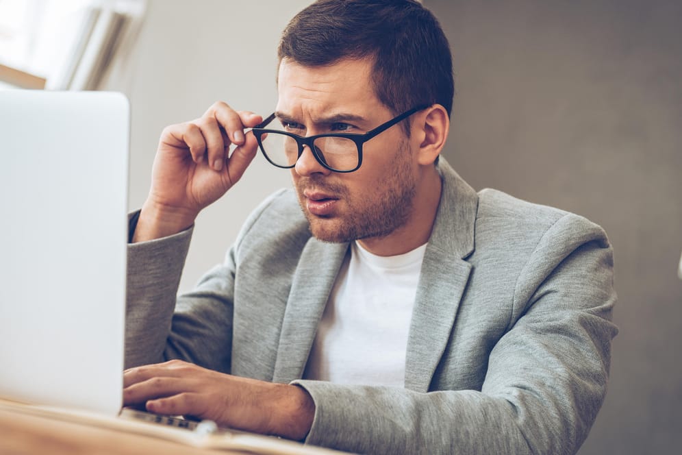 Ein Mann schaut über den Rand seiner Brille auf den Laptop-Bildschirm: Sind Sie ein Phishing-Experte? Machen Sie den Test!