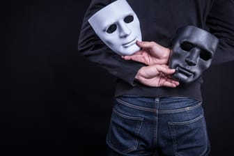 Ein Mann hält zwei Masken hinter dem Rücken: Identitätsdiebstahl im Internet passiert häufiger, als viele denken.