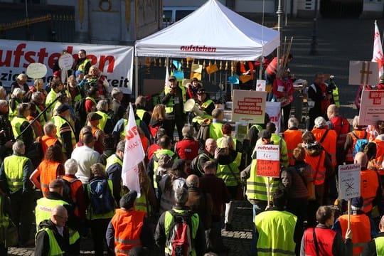 Demonstranten in bunten Westen stehen vor dem Düsseldorfer Rathaus.