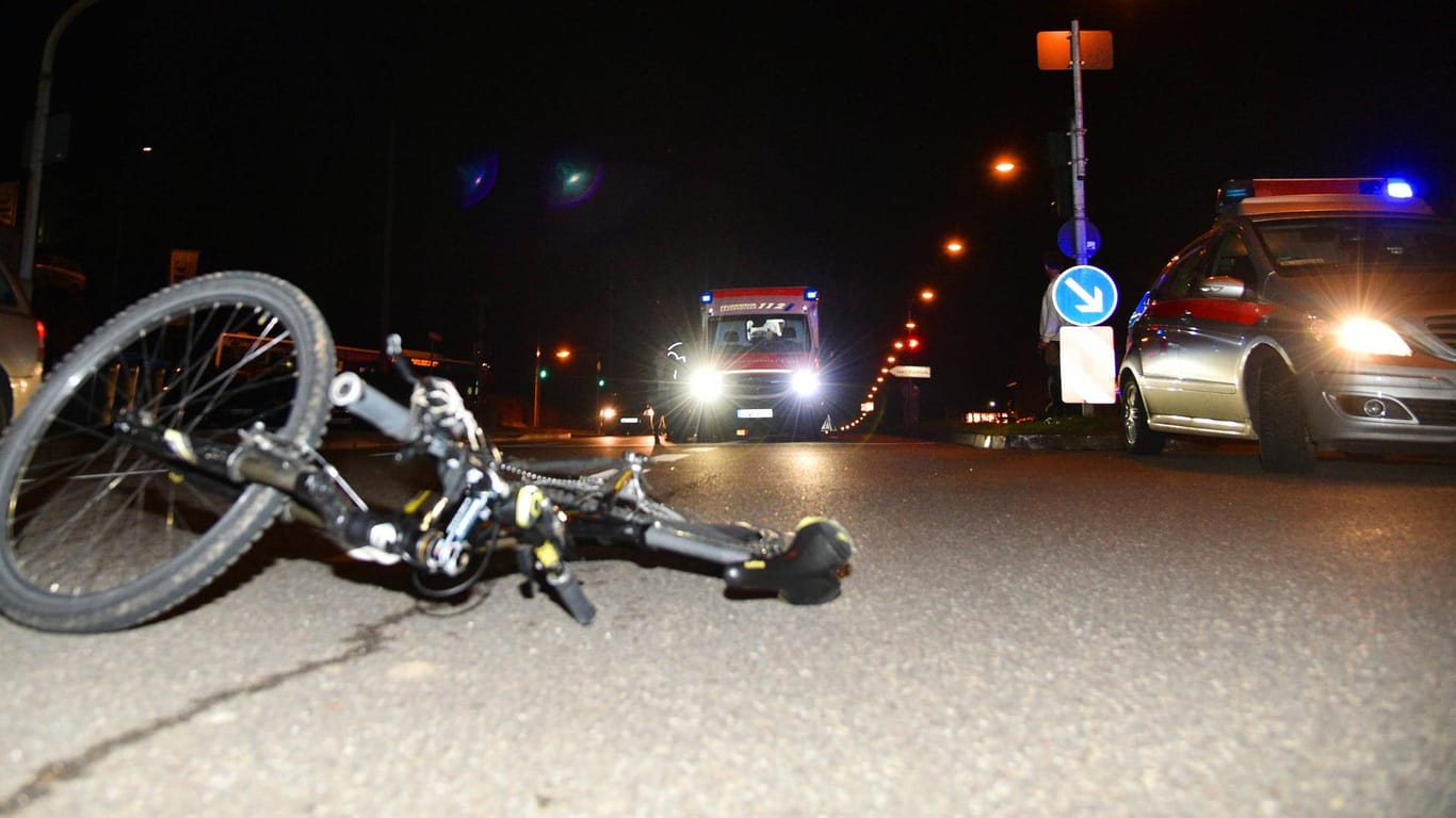 Fahrrad liegt bei Nacht auf der Straße, Rettungs- und Polizeiwagen im Hintergrund: Nach dem Angriff alarmierte die Radfahrerin den Rettungsdienst und wurde noch in der Nacht operiert.