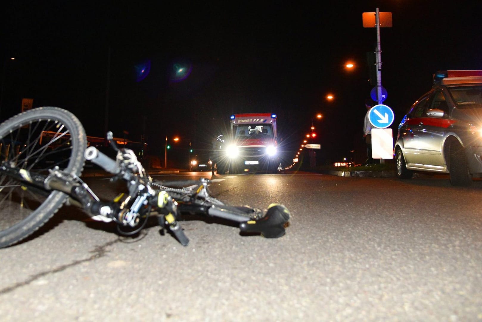 Fahrrad liegt bei Nacht auf der Straße, Rettungs- und Polizeiwagen im Hintergrund: Nach dem Angriff alarmierte die Radfahrerin den Rettungsdienst und wurde noch in der Nacht operiert.