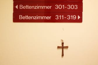 Ein kleines Holzkreuz hängt unter Hinweisschildern auf einer Station in einem kirchlichen Krankenhaus.