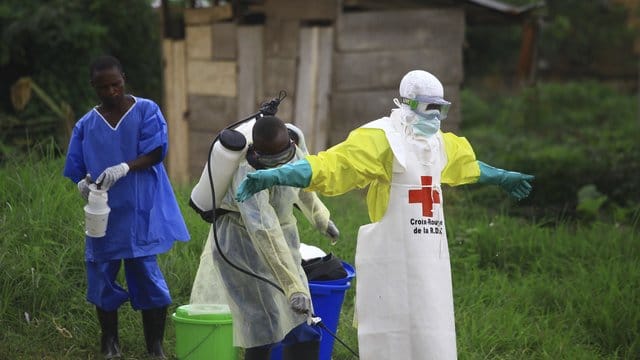 Ein Helfer des Roten Kreuzes wird nach einem Einsatz in einem Ebola-Behandlungszentrum von einem Kollegen mit Desinfektionsmittel eingesprüht. Ein Helfer des Roten Kreuzes wird nach einem Einsatz in einem Ebola-Behandlungszentrum von einem Kollegen mit Desinfektionsmittel eingesprüht.