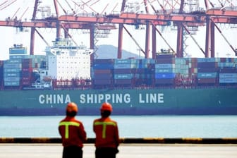 Hafenarbeiter beobachten im Hafen von Qingdao die Beladung eines Containerschiffs.