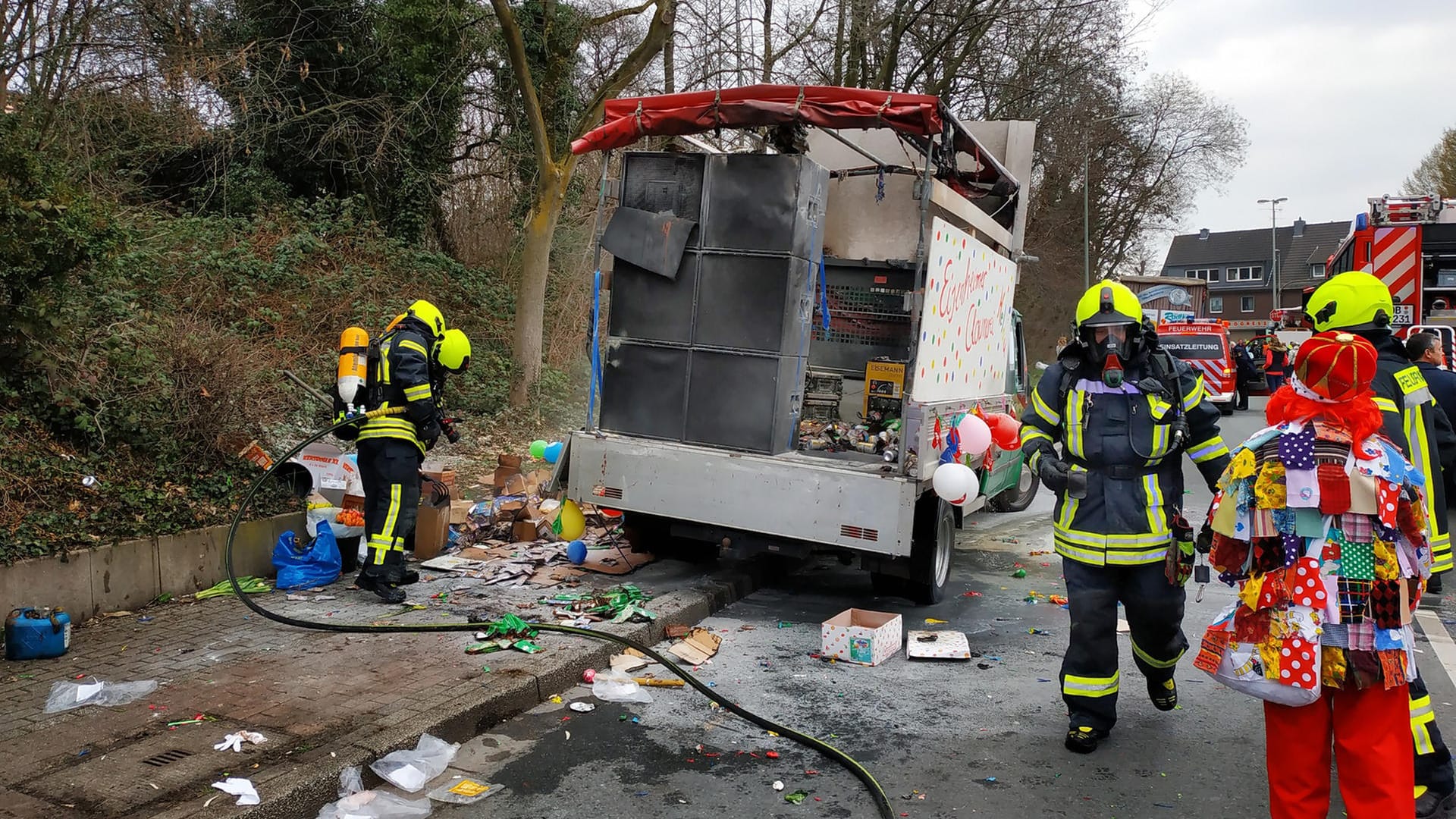 Feuerwehrleute sind bei einem ausgebrannten Karnevalswagen im Einsatz: Fünf Helfer verletzten sich, als sie den Brand löschen wollten.