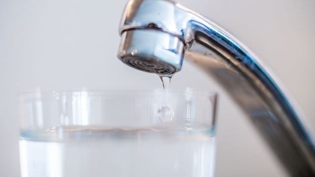 Wasser läuft aus einem Wasserhahn in ein Glas.