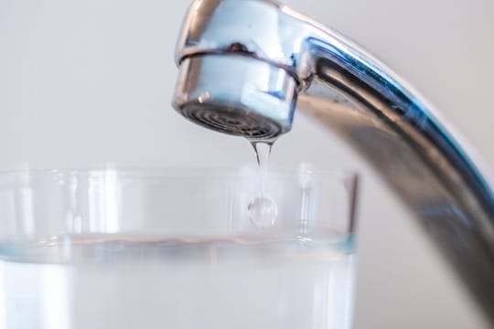 Wasser läuft aus einem Wasserhahn in ein Glas.