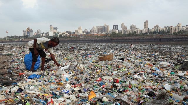 Ein Mann sammelt Plastik und andere wiederverwertbare Materialen an der von Plastiktüten und sonstigen Müll übersäten Küste vor Mumbai.