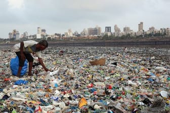 Ein Mann sammelt Plastik und andere wiederverwertbare Materialen an der von Plastiktüten und sonstigen Müll übersäten Küste vor Mumbai.