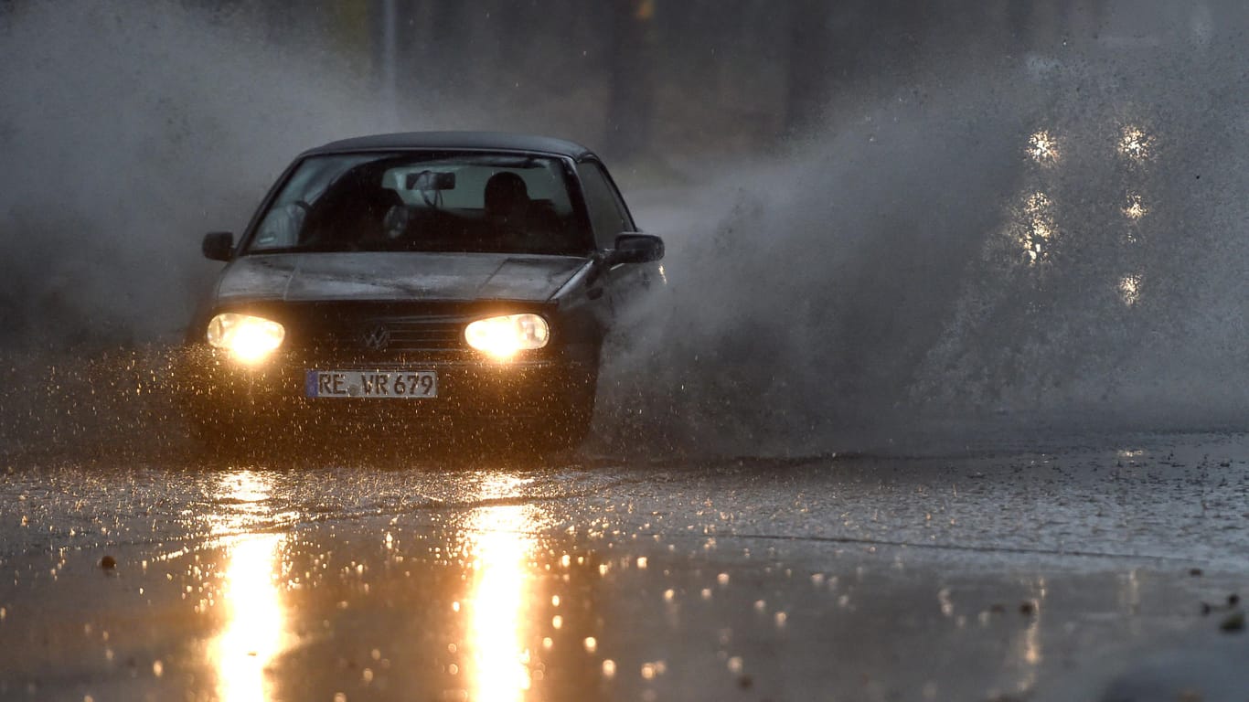 Straße in Gelsenkirchen: Ein Auto fährt durch eine tiefe Pfütze, die sich durch Starkregen auf einer Straße gebildet hat.
