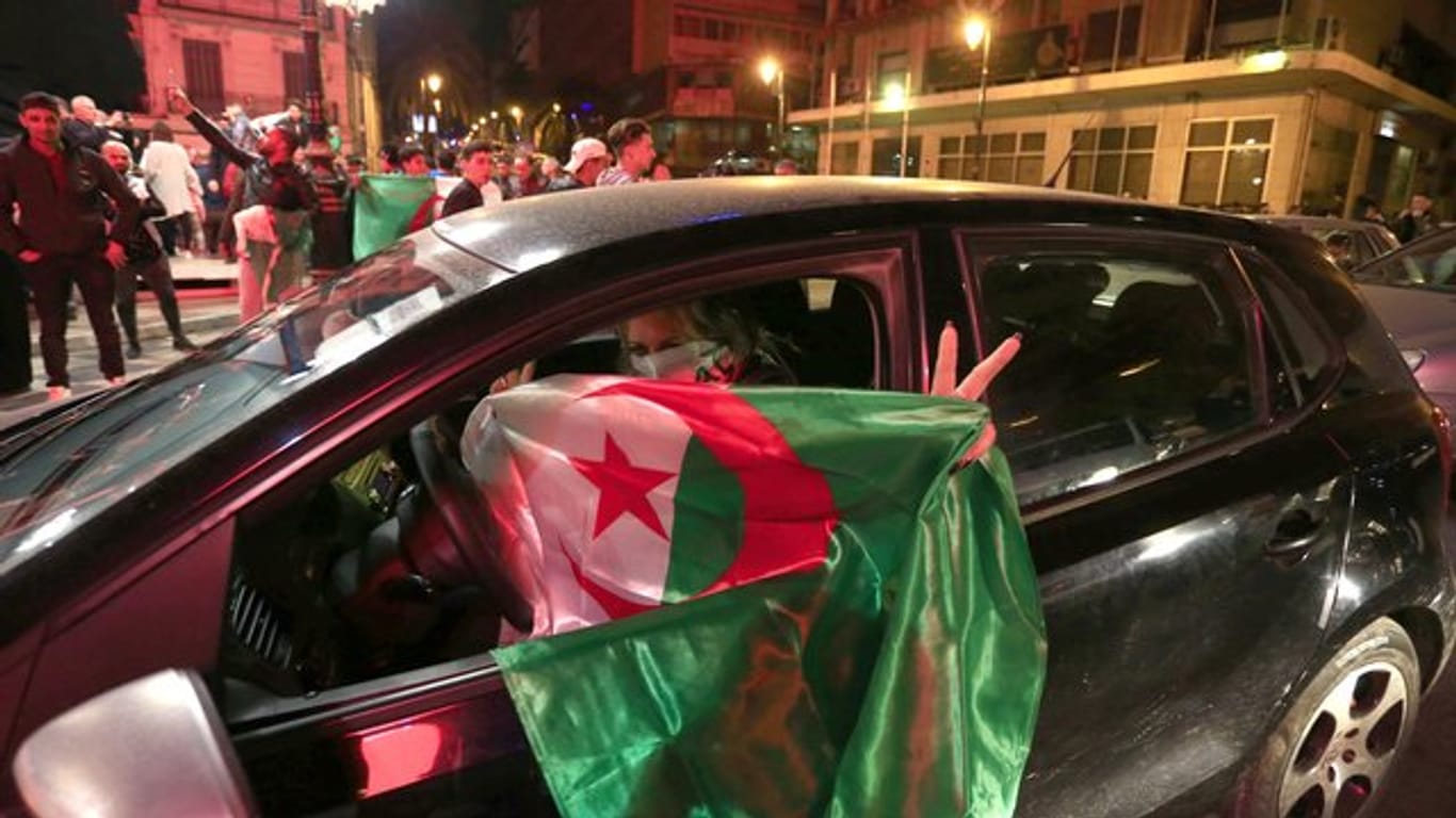 Eine Frau hält in Algier eine algerische Nationalflagge aus ihrem Auto, während im Hintergrund Menschen in den Straßen feiern.