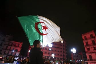 Ein Algerier schwenkt eine Nationalflagge, während Menschen feiern, nachdem Präsident Bouteflika angekündigt hat, dass er auf eine weitere Kandidatur verzichtet.