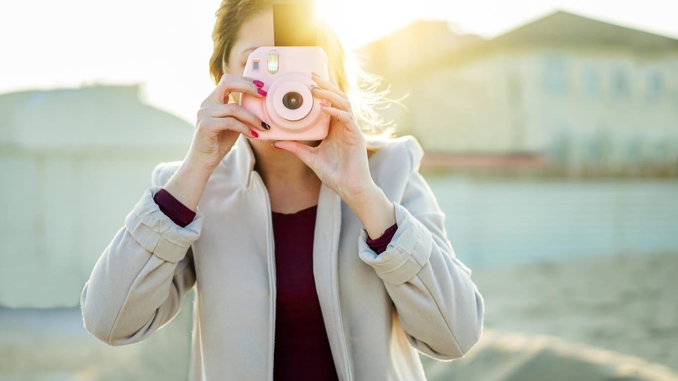 Eine Frau macht mit einer Sofortbildkamera ein Foto am Strand von Rimini.