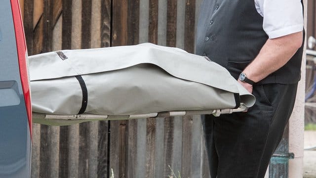 Ein Bestatter schiebt einen Sarg in einen Leichenwagen. Ein Bestatter schiebt einen Sarg in einen Leichenwagen.