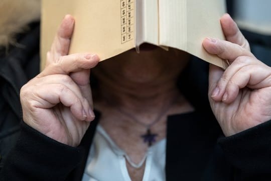 Die Angeklagte hält sich im Gerichtssaal eine Mappe vors Gesicht
