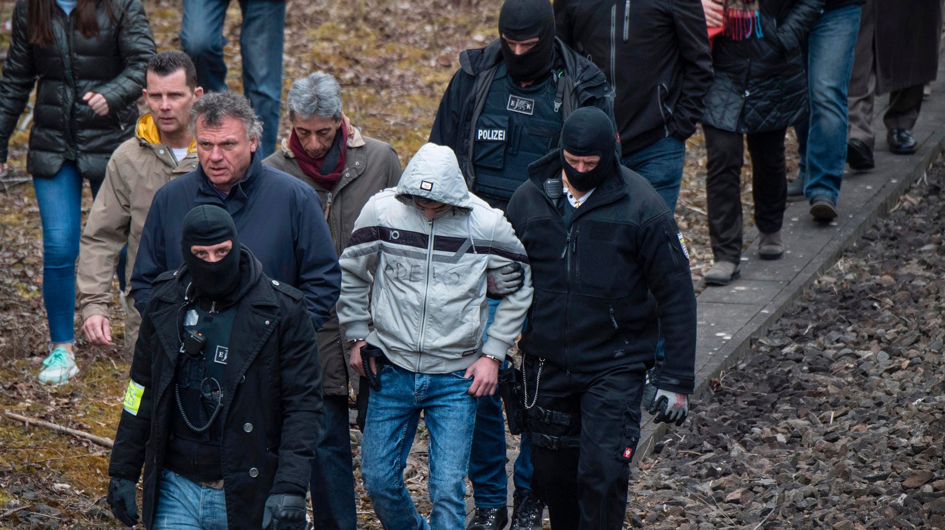 Hessen, Wiesbaden: Begleitet von zwei maskierten Polizeibeamten wird der wegen Mordes an der 14-jährigens Susanna angeklagte Ali B. entlang einer Eisenbahnstrecke bei Erbenheim geführt.