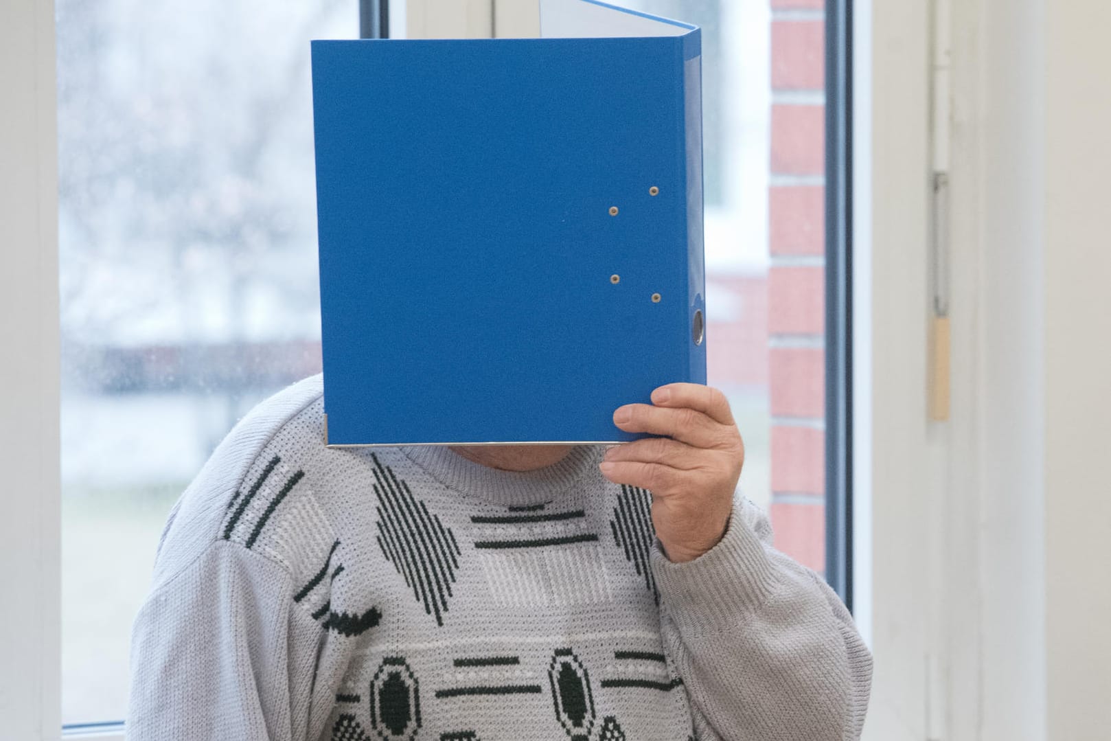 Stralsund: Der Angeklagte hält sich im Sitzungssaal einen Aktenordner vor das Gesicht.