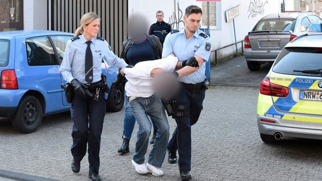 Ein mutmaßlich Verdächtiger wird von Polizeibeamten abgeführt, im Hintergrund eine Zivilfahnderin der Polizei. Ein mutmaßlich Verdächtiger wird von Polizeibeamten abgeführt, im Hintergrund eine Zivilfahnderin der Polizei.