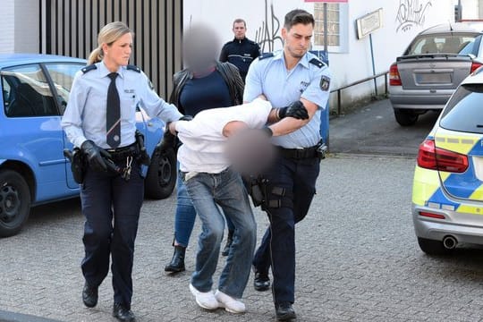 Ein mutmaßlich Verdächtiger wird von Polizeibeamten abgeführt, im Hintergrund eine Zivilfahnderin der Polizei.