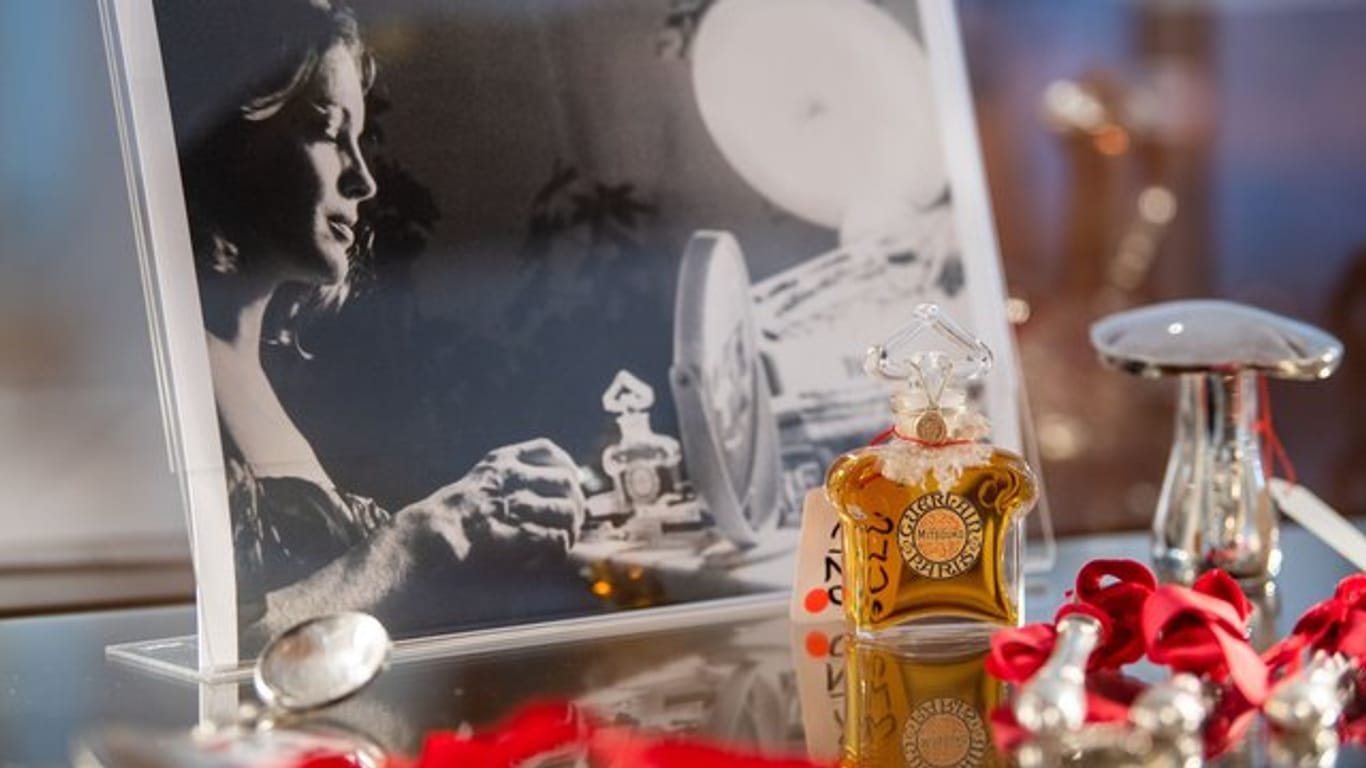 Ein Parfumflacon steht in einer Vitrine vor einem Foto von Romy Schneider.