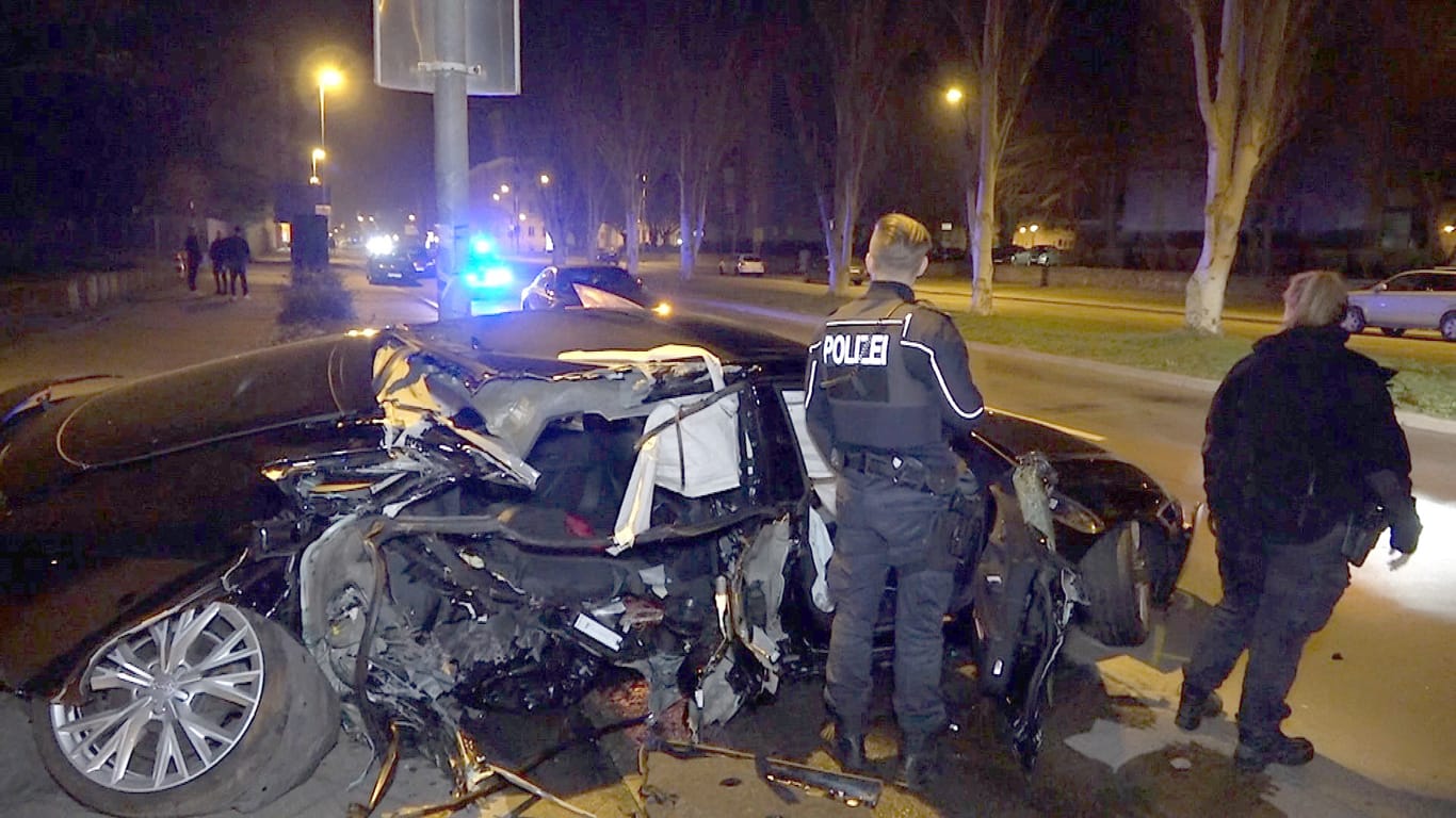 Polizisten stehen an einem völlig demolierten Auto in Magdeburg