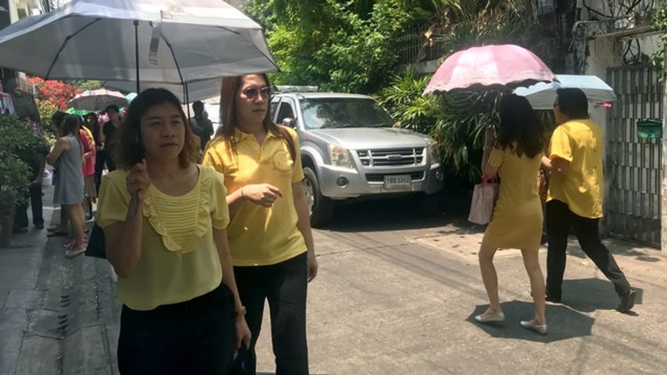 Passanten in gelber Kleidung auf einer Straße in der Hauptstadt Bangkok.