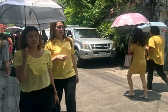 Passanten in gelber Kleidung auf einer Straße in der Hauptstadt Bangkok.