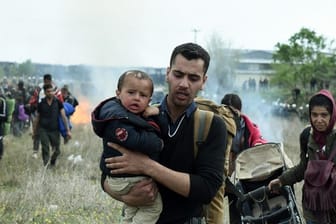Ein Mann hält ein Baby auf dem Arm, während die Bereitschaftspolizei Tränengas einsetzt.