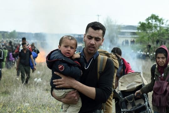 Ein Mann hält ein Baby auf dem Arm, während die Bereitschaftspolizei Tränengas einsetzt.