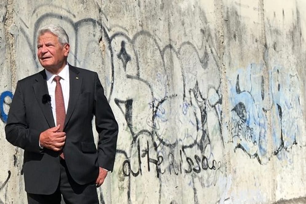 Der ehemalige Bundespräsident Joachim Gauck steht neben Überresten der Mauerin Berlin.