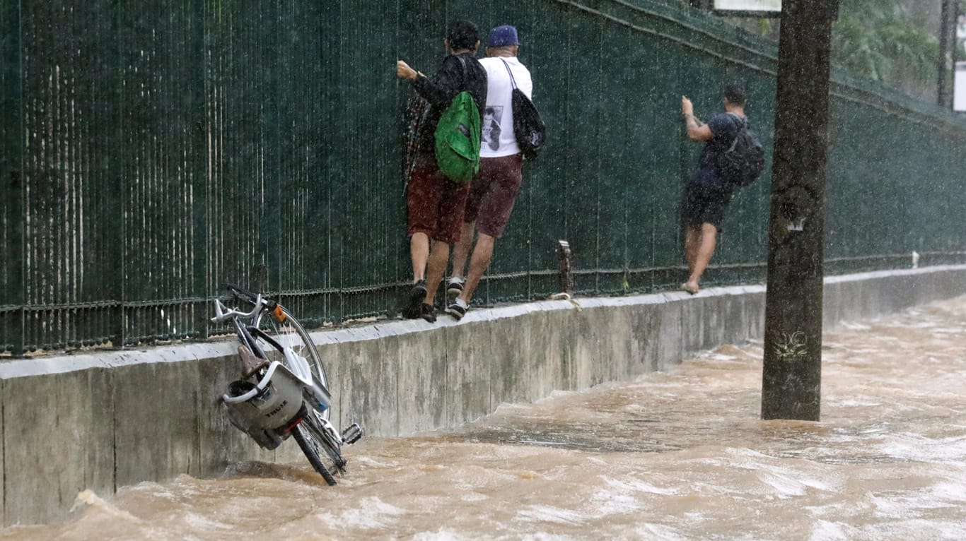 Fußgänger klettern an einem Zaun entlang, um sich vor dem Wasser zu retten: Die Regenfälle lösten Erdrutsche aus und ließen Bäume umstürzen.
