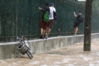 Fußgänger klettern an einem Zaun entlang, um sich vor dem Wasser zu retten: Die Regenfälle lösten Erdrutsche aus und ließen Bäume umstürzen.