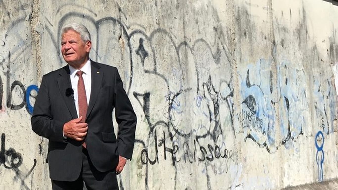 Der ehemalige Bundespräsident Joachim Gauck steht neben Überresten der Mauer in Berlin.