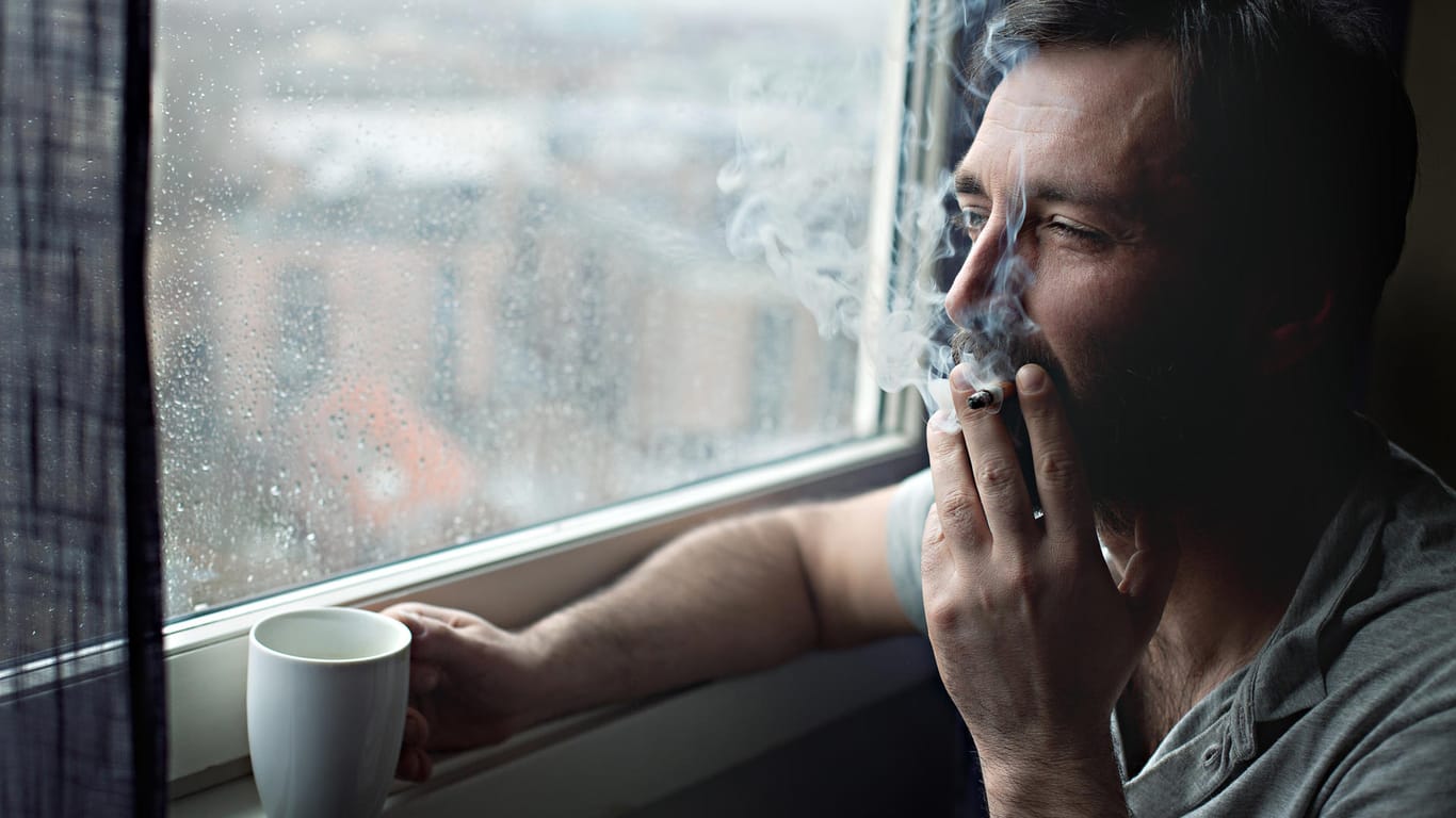 Raucher steht am Fenster: Neben der Krebsgefahr, die von Zigaretten ausgeht, ist auch das Risiko für Erkrankungen von Herz und Gefäßsystem erhöht.