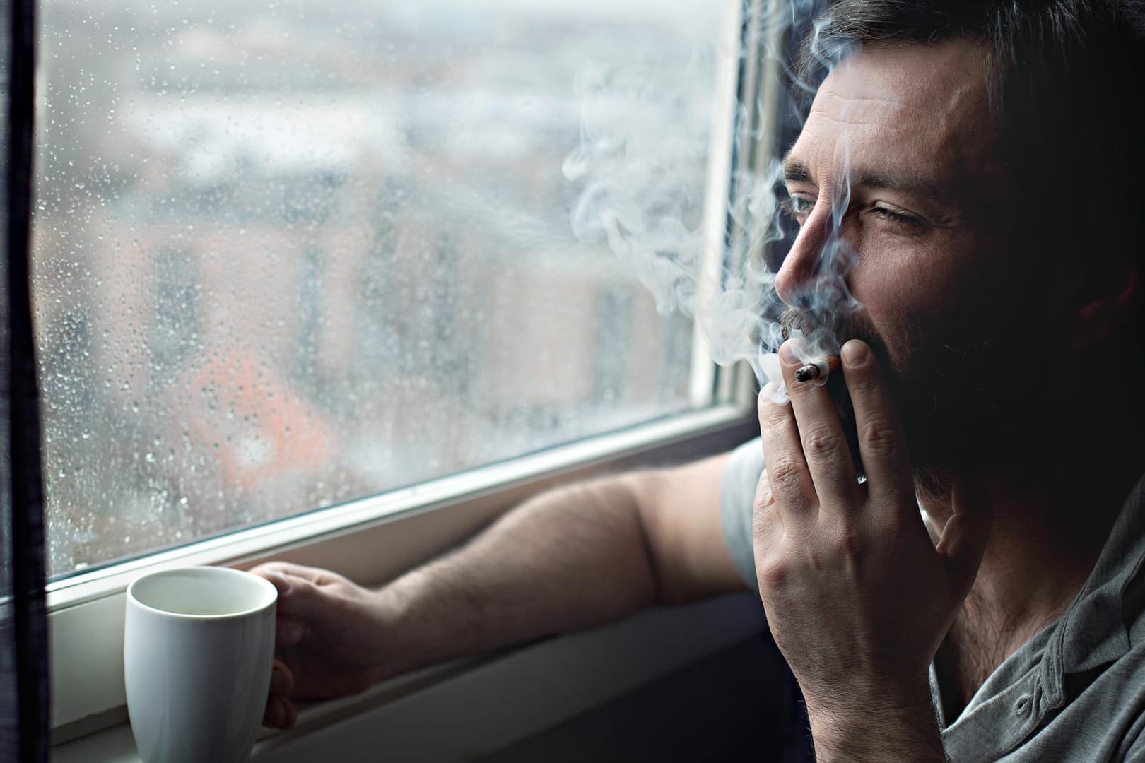 Raucher steht am Fenster: Neben der Krebsgefahr, die von Zigaretten ausgeht, ist auch das Risiko für Erkrankungen von Herz und Gefäßsystem erhöht.