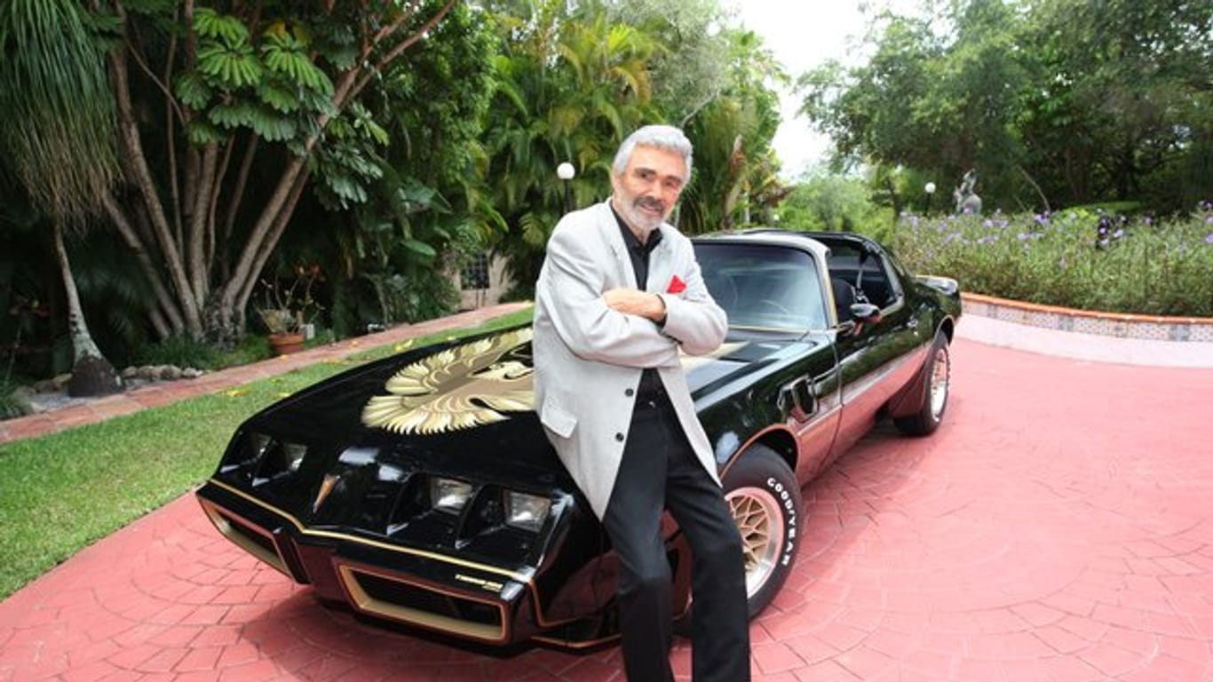 Schauspielers Burt Reynolds steht an seinem schwarz-goldenen Sportwagen der Marke Pontiac Trans Am (1979).