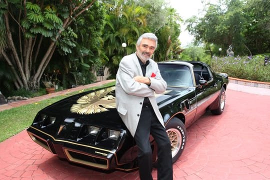 Schauspielers Burt Reynolds steht an seinem schwarz-goldenen Sportwagen der Marke Pontiac Trans Am (1979).