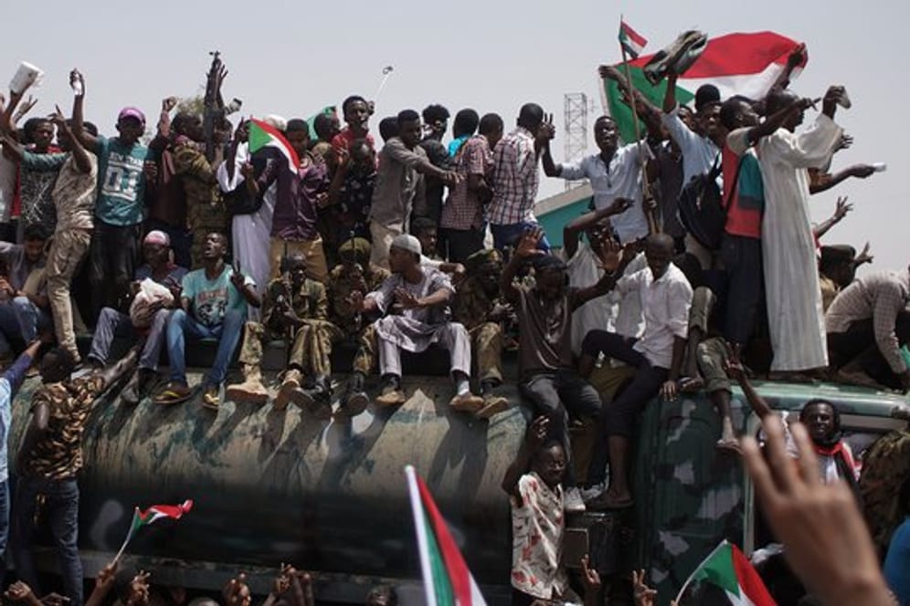 Demonstranten und Soldaten sitzen und stehen auf einem Militärfahrzeug vor dem Verteidigungsministerium in Khartum.