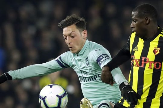 Arsenal-Spieler Mesut Özil (l) behauptet sich gegen Abdoulaye Doucoure vom FC Watford beim Kampf um den Ball.