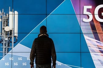 Ein Mann steht im Gebäude der Bundesnetzagentur vor einer Leinwand mit der Aufschrift "5G".